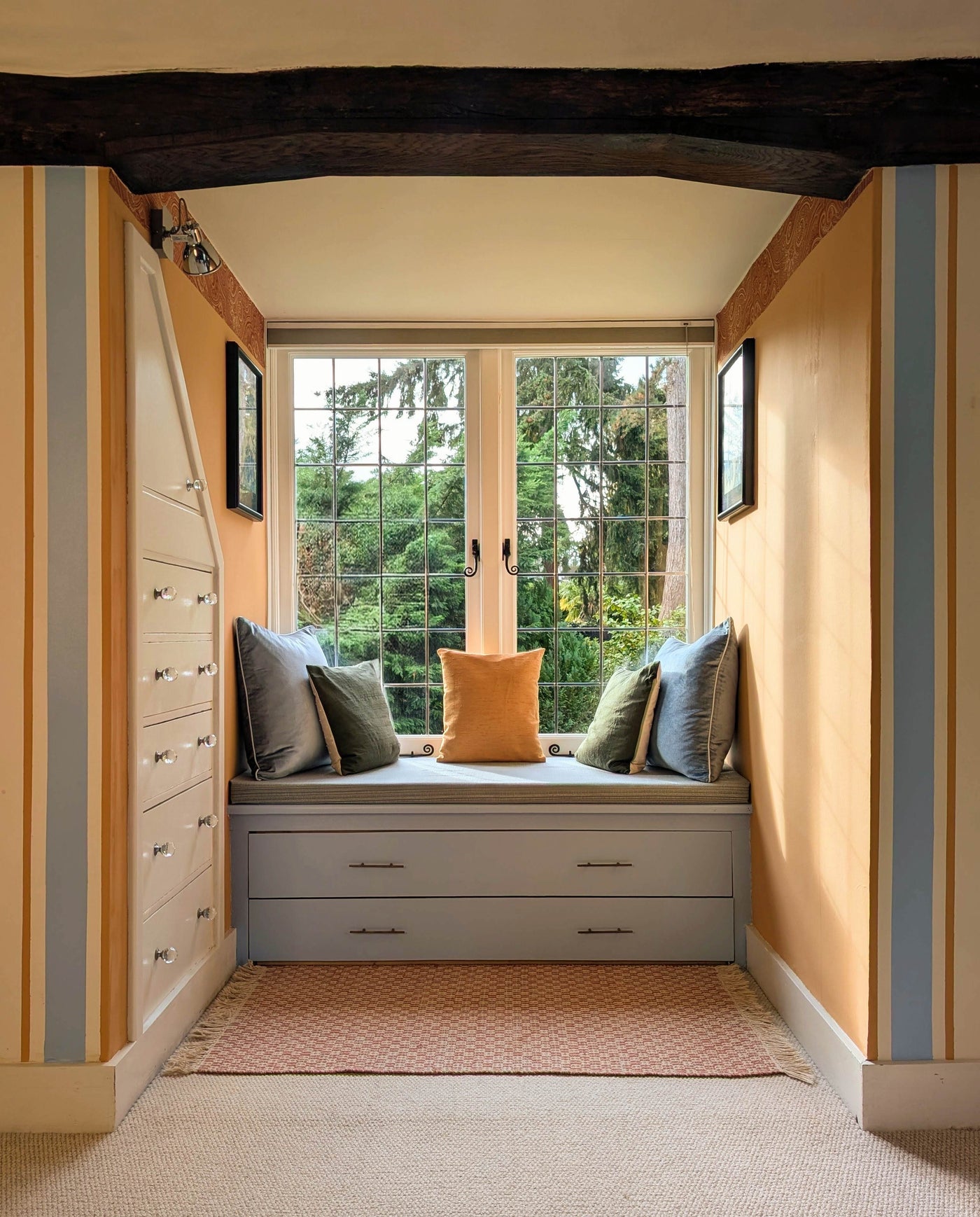 Room with striped walls, a window seat with pillows, and wooden beams.