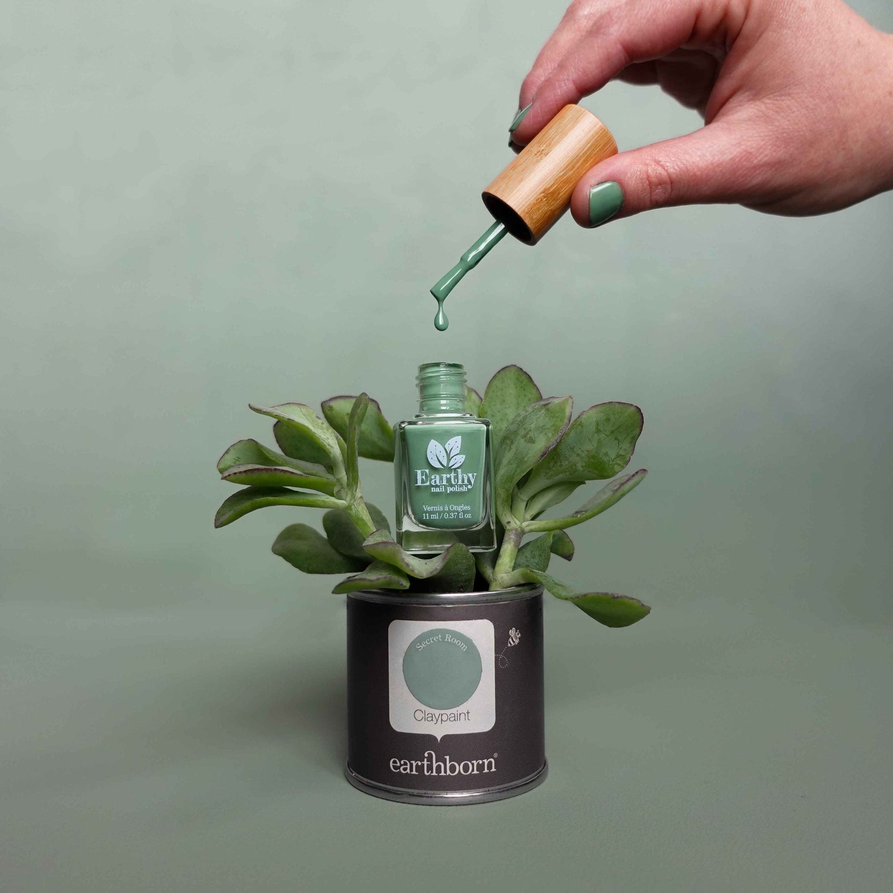 Green nail polish sitting in a plant that is potted in a small Earthborn paint tin.|Rose used as paint brush in Earthborn paint tin with Maya's Rose Earthy Nail Polish. Earthborn paint brush dipped in Icelandic Blue Earthy Nail polish.|Paint brush drippin