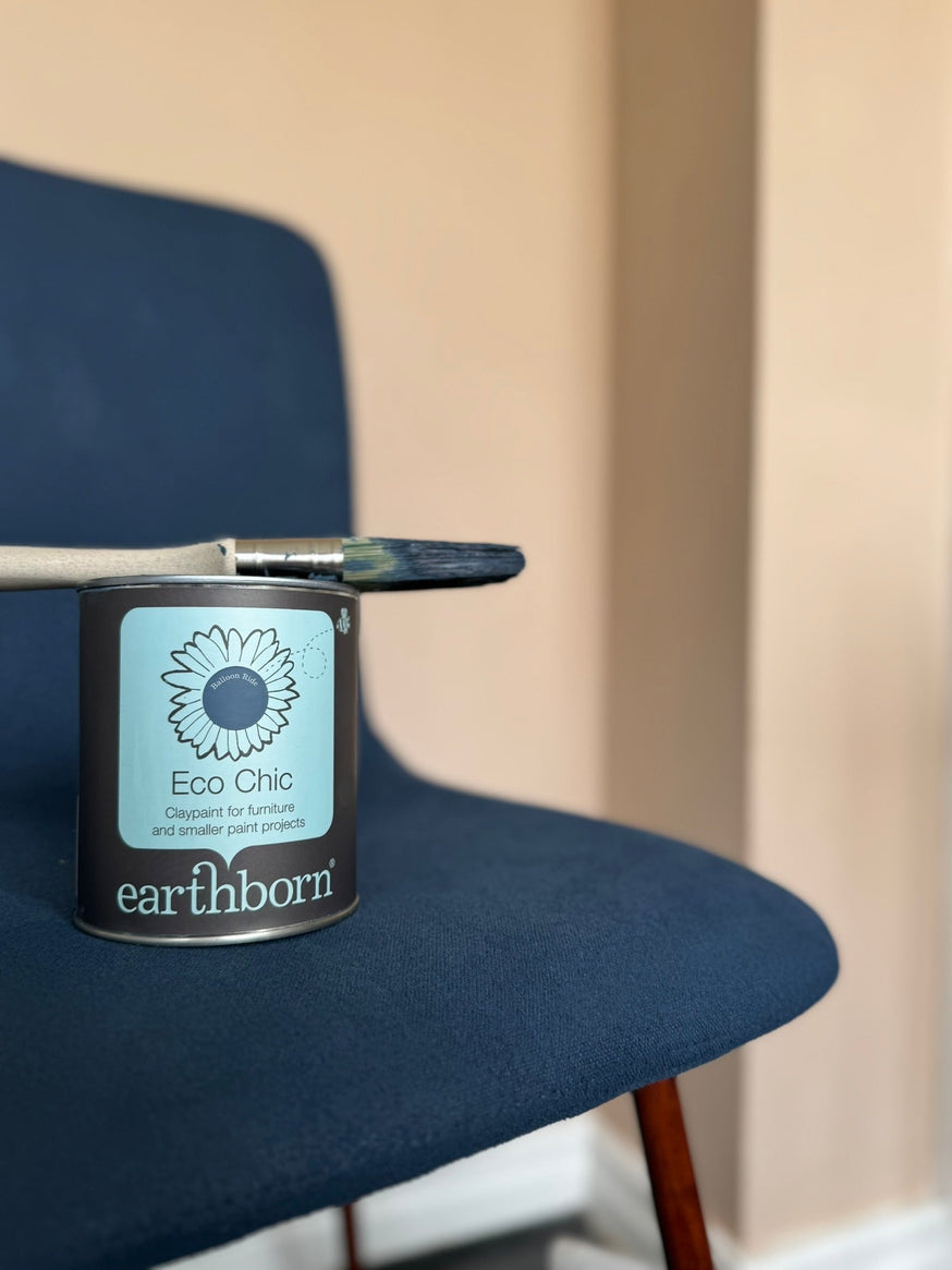 A tin of Earthborn Eco Chic and a used paintbrush on a fabric chair that's been painted with Eco Chic in the colour Balloon Ride.|A before image of a grey fabric chair.|Placing masking tape around the leg of a fabric chair.|Spraying water from a spray bot