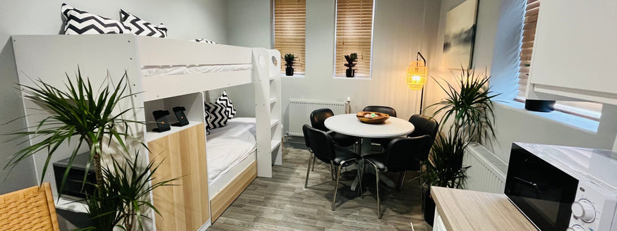 Close up of an open plan apartment and living space.|Blackpool Victoria Hospital breakroom and kitchen open plan.|A dark haired lady painting a table's legs white while sitting on a protective sheet.|Small grey open plan apartment, showing good usage of s