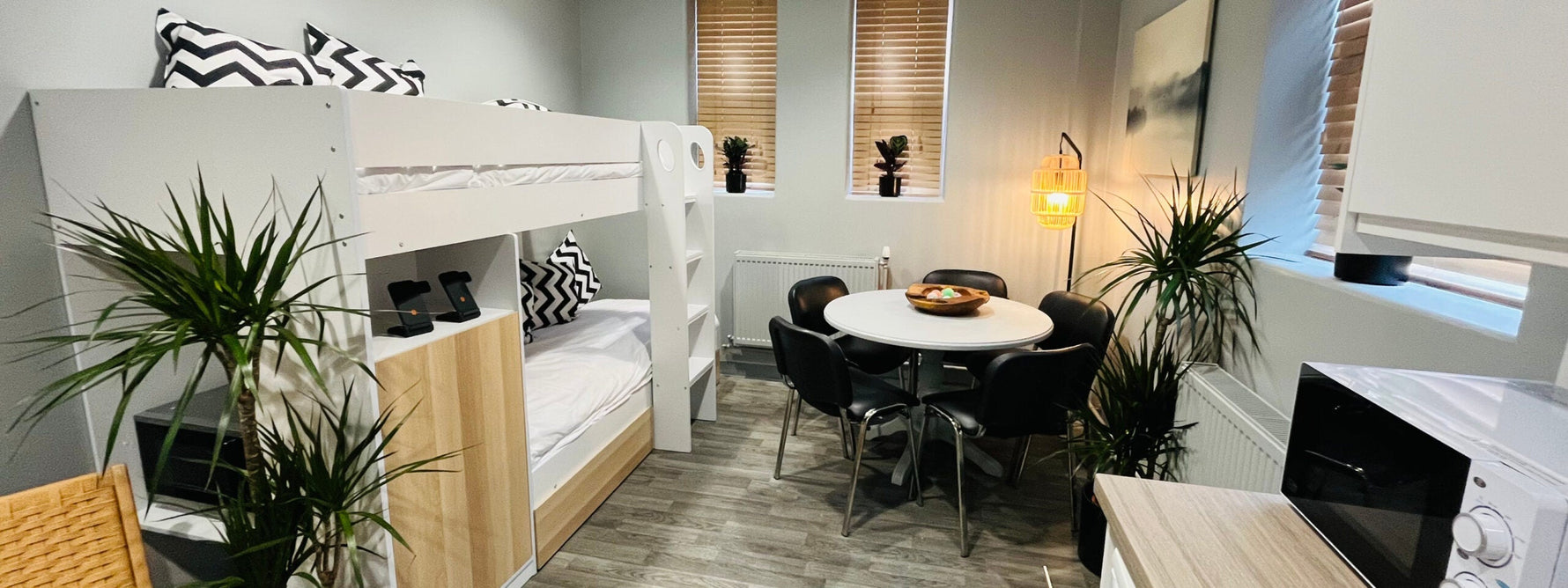 Close up of an open plan apartment and living space.|Blackpool Victoria Hospital breakroom and kitchen open plan.|A dark haired lady painting a table's legs white while sitting on a protective sheet.|Small grey open plan apartment, showing good usage of s