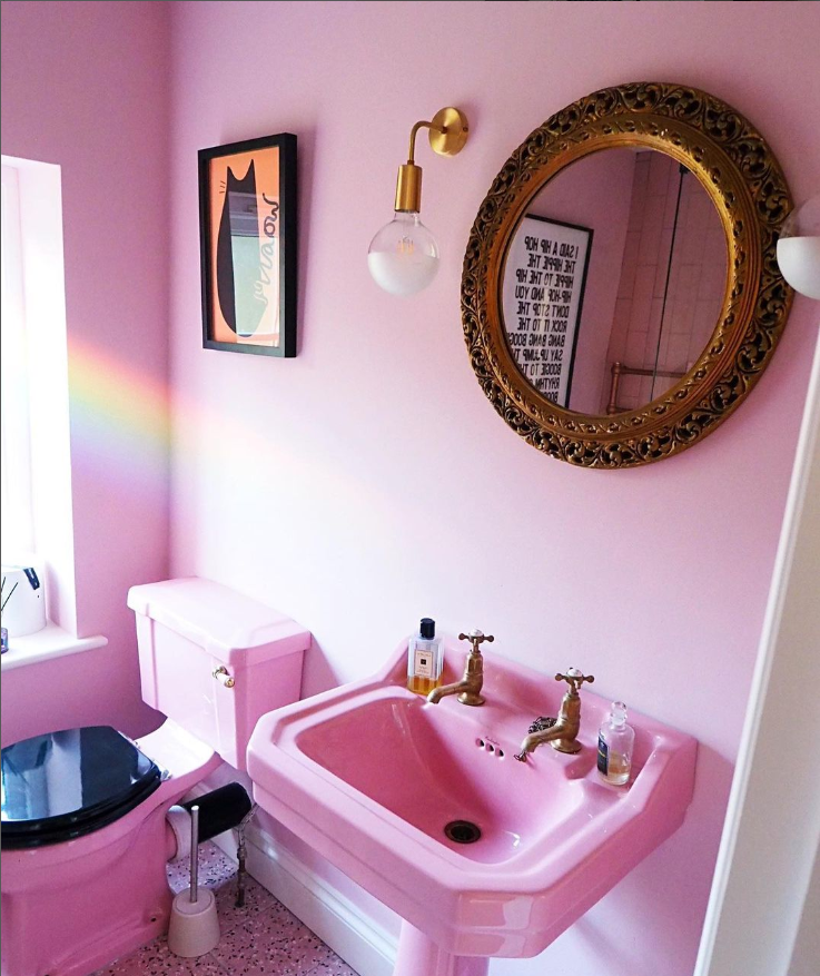 Pink bathroom with gold accents and mirror.|Brightly decorated wall and table with books stacked underneath, a vase and candle on top of the table.|Little girls bedroom with pale pink decorations and soft toys.|Old cottage with blue skies, a front garden