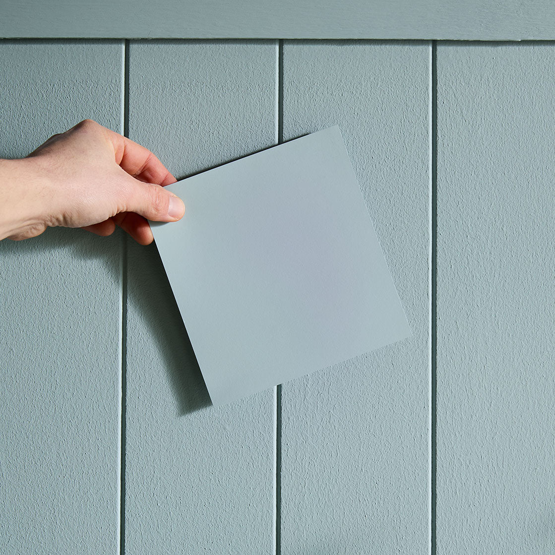 Hand holding a color swatch to a wall.