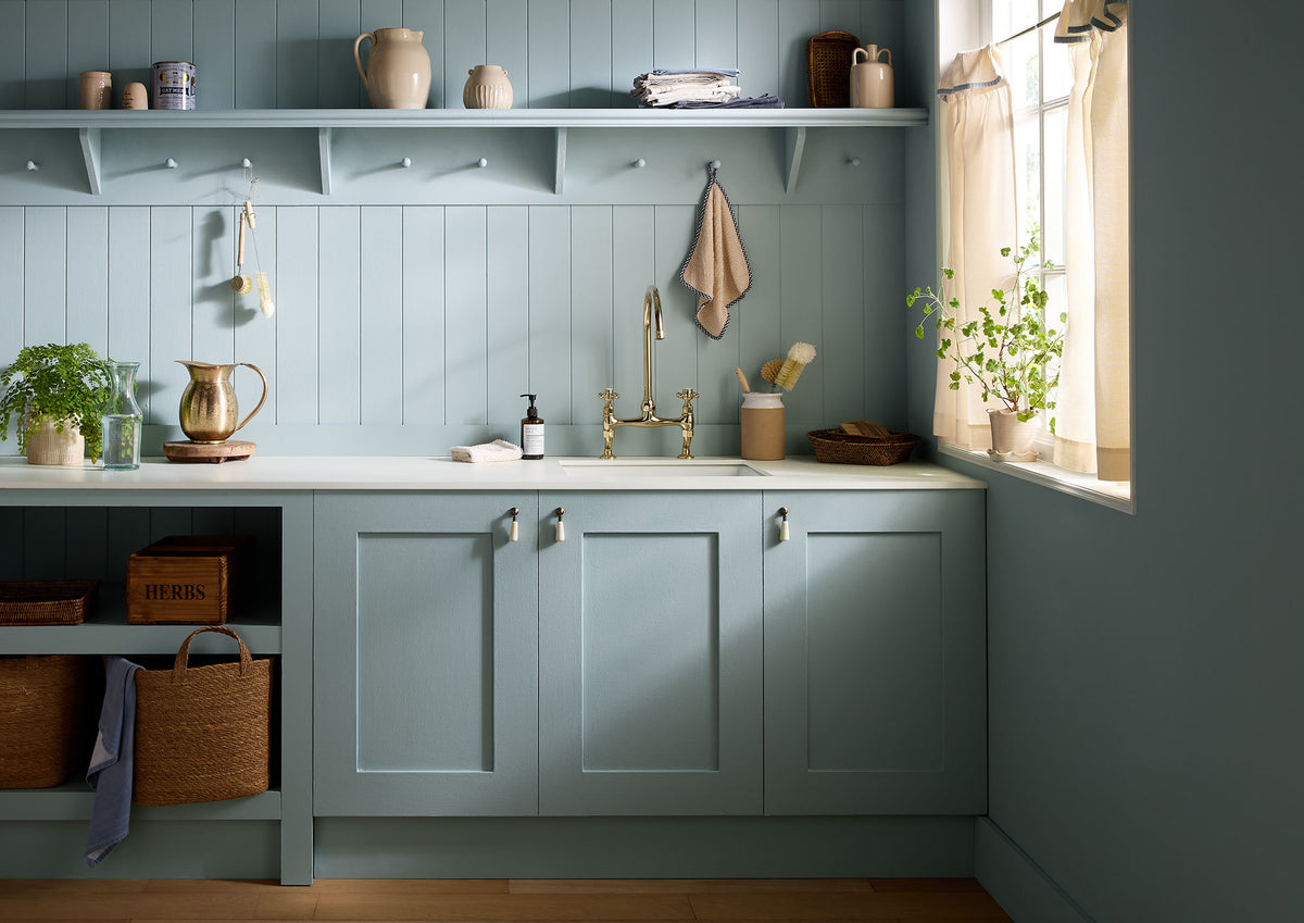 Modern kitchen with blue cabinets, white countertop, and window with light curtains.