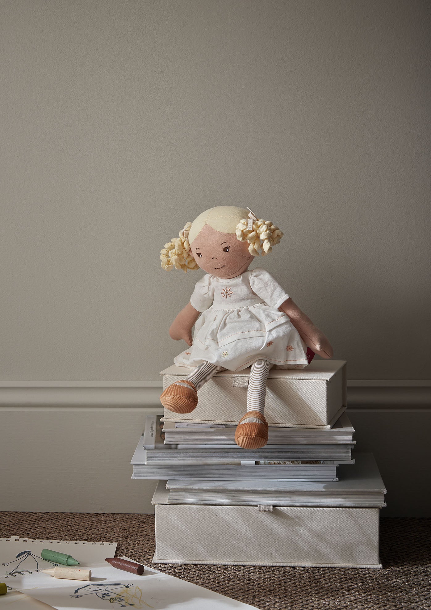 Stuffed doll with blonde hair sitting on a stack of books against a plain wall.