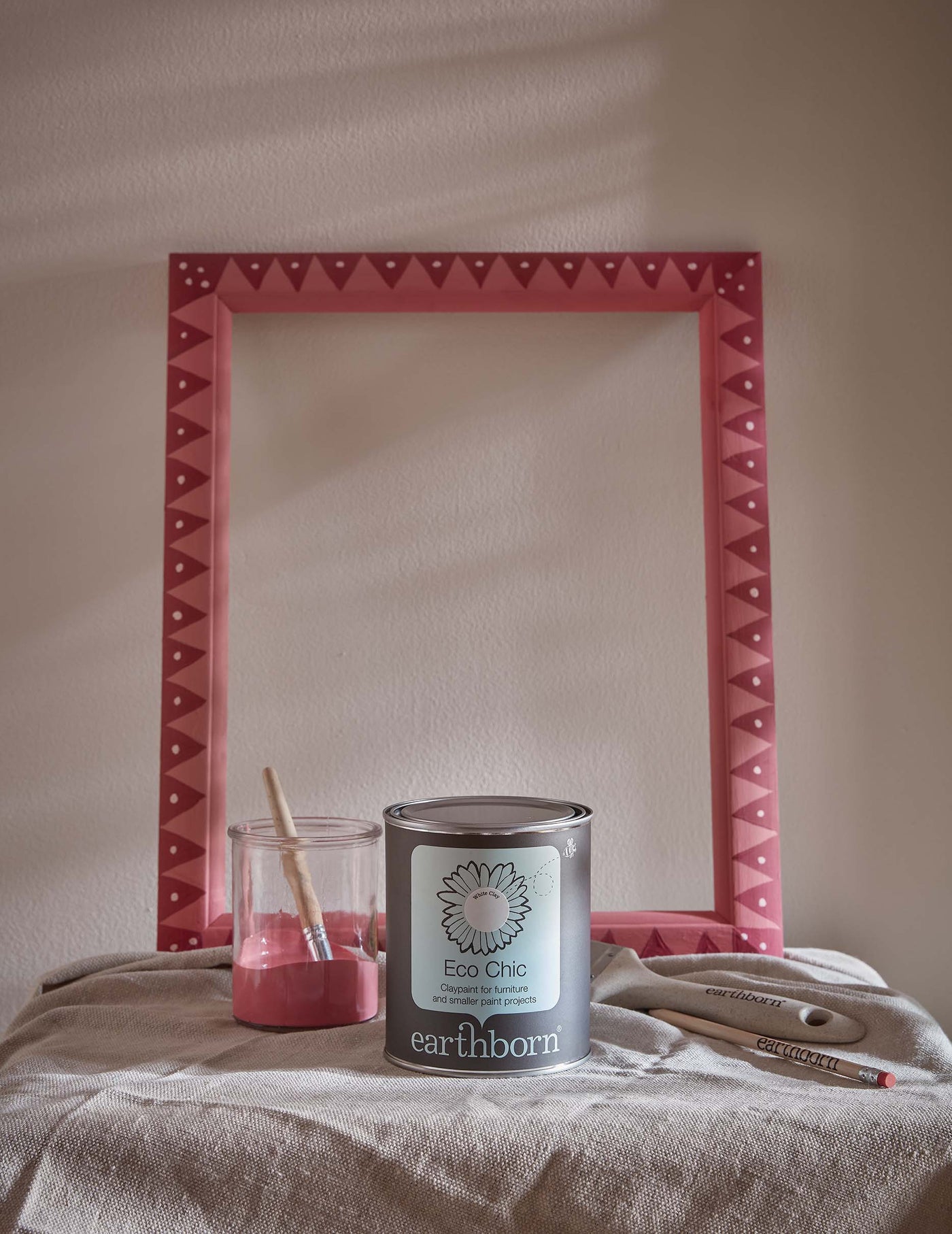Tin of Earthborn Eco Chic paint with a pink decorative framein the background