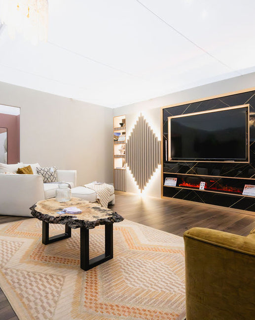 A modern living room interior featuring a large black TV mounted on a dark marble-patterned wall with gold trim, a geometric patterned rug, a rustic live-edge wood coffee table, and a white sofa in the background.
