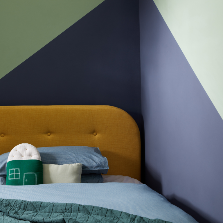 The corner of a bedroom with both walls painted using a colour block in blue and green.