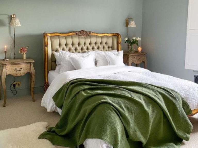 A bed against a pale wall with white linen and a green throw.