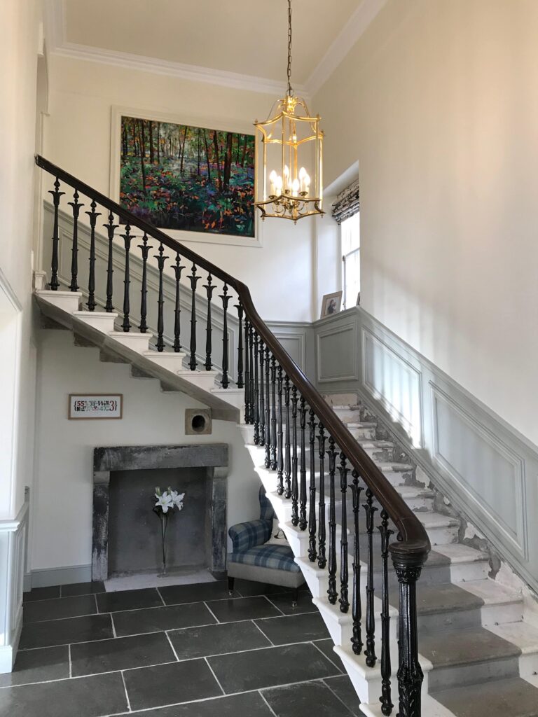 A stair case with an old with a low hanging gold light and grey slate tiles.