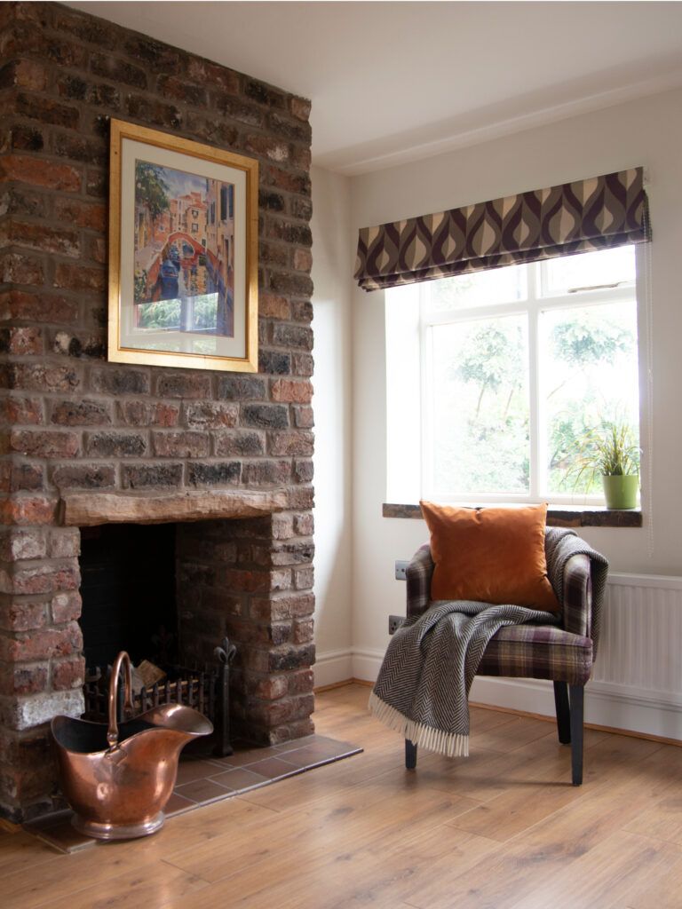 A raw brick fireplace with a tartan armchair and large window.