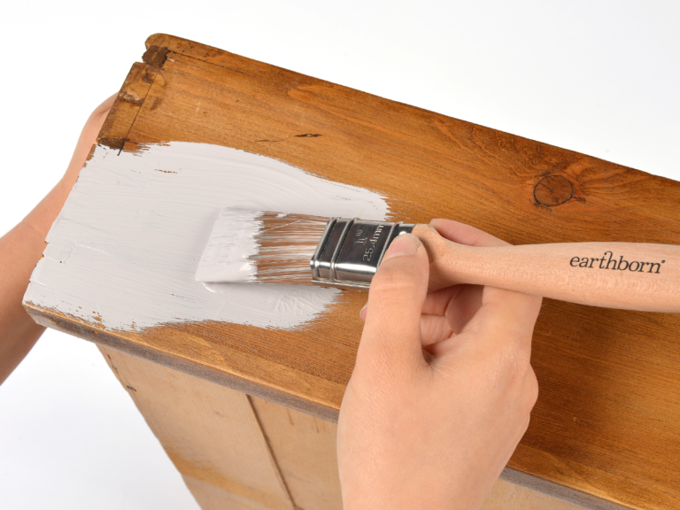 Close up of hands painting a wooden draw using an Earthborn paint brush.