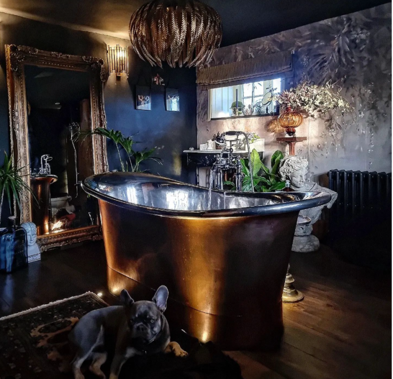 Dark bathroom with a free standing bath tub and a French Bulldog sitting on the carpet.