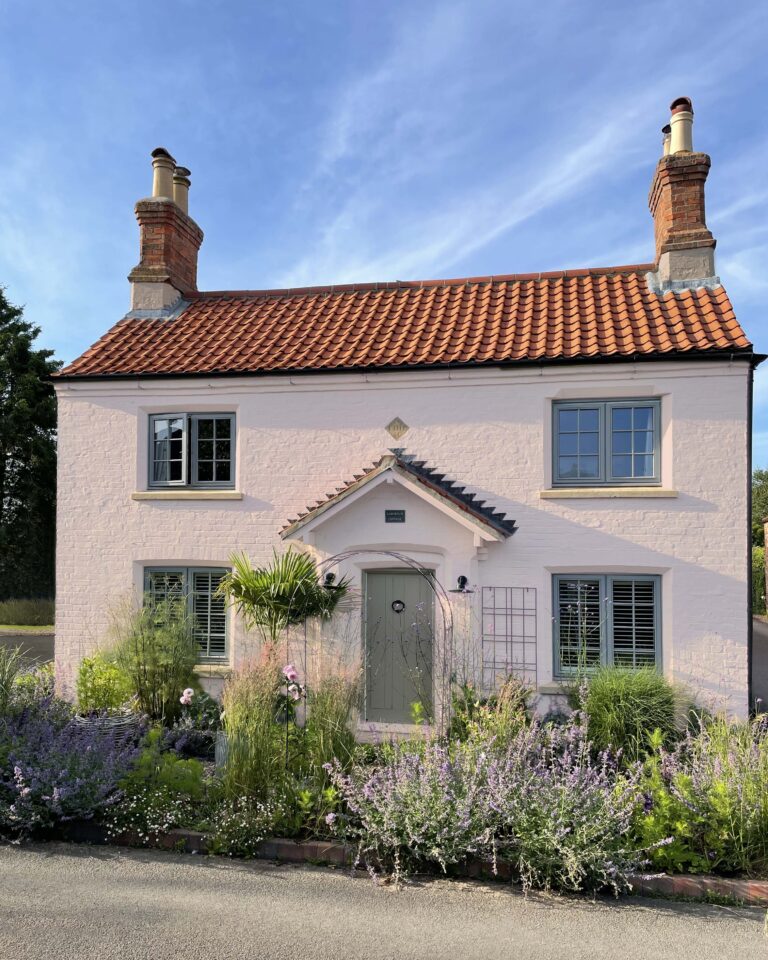 Old cottage with blue skies, a front garden and the road.