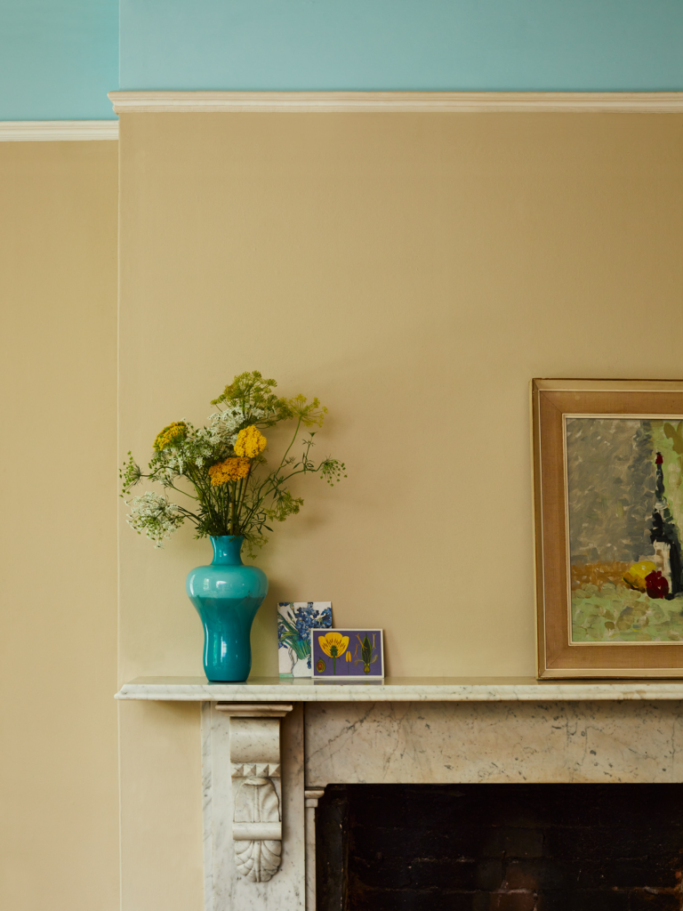 Mantel piece above a stone fire place with a painting and vase of flowers.